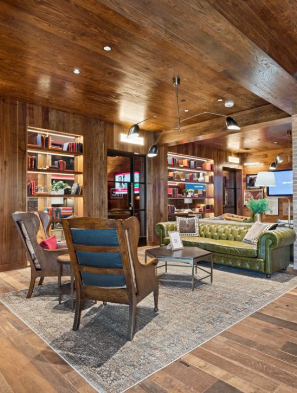 Lounge area with wood paneled walls, a green leather sofa, and two armchairs on an area rug.