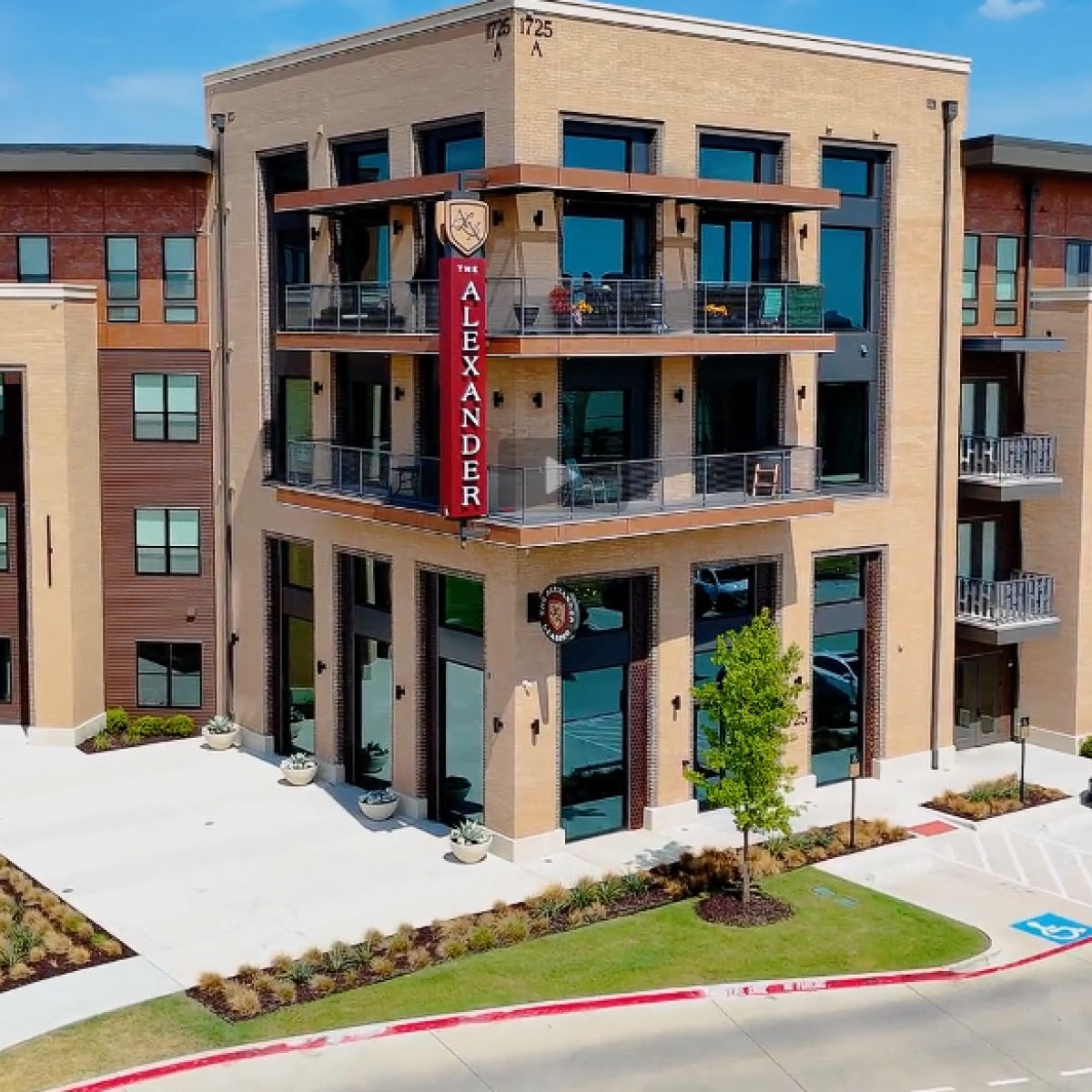 Aerial view of The Alexander apartment complex, a multi-story brick building with balconies and a parking lot.