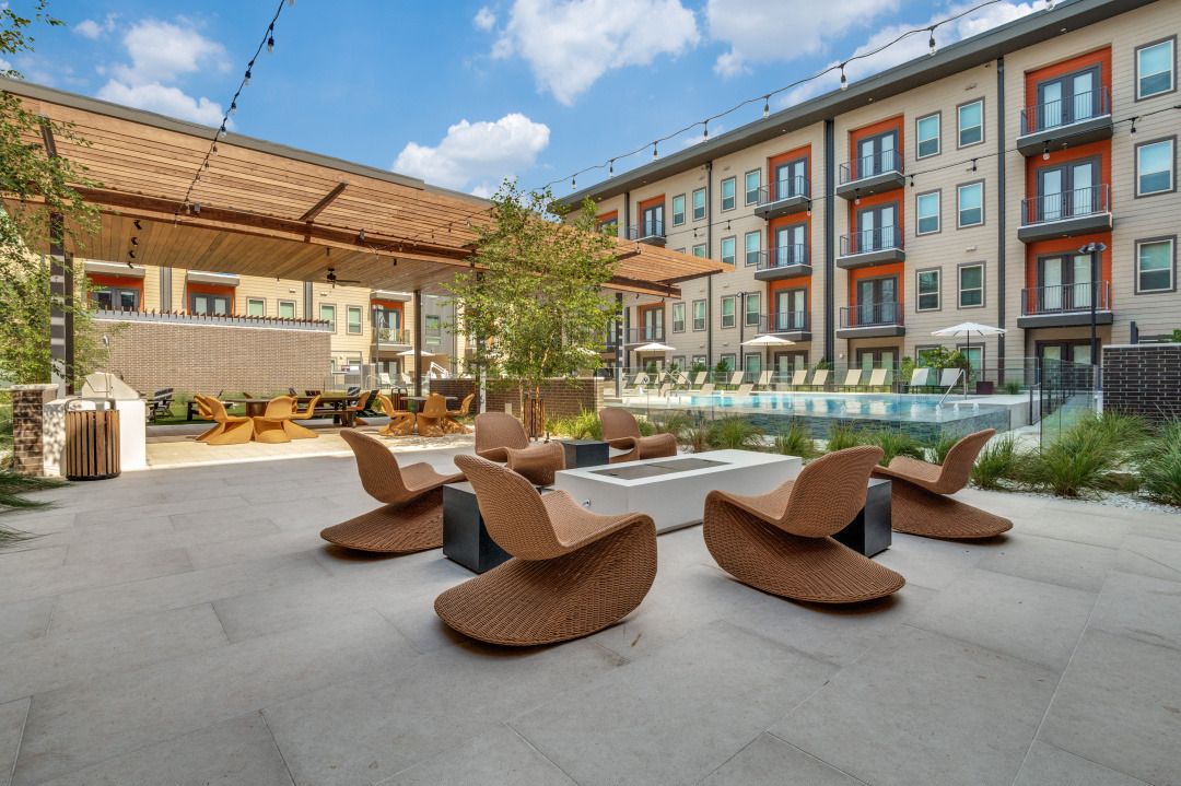 Outdoor apartment courtyard with a swimming pool, covered patio, and lounge chairs arranged around a fire pit.